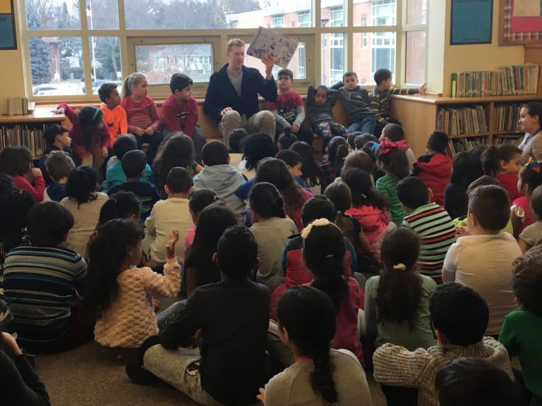 Brian Scalabrine seated, holding up a book, talking to a group of children in a library