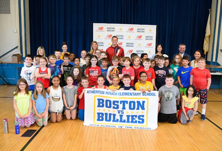 A group of students and adults in standing together holding up a Boston vs. Bullies large poster smiling at the camera.