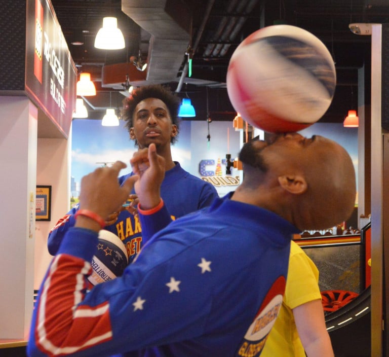 Two Harlem Globetrotters, one holding a basketball and another spinning a basketball on his nose