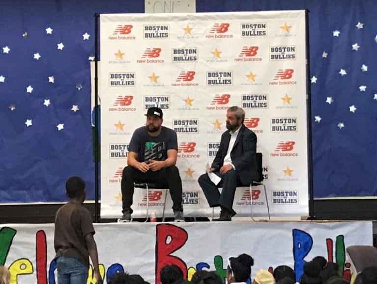 Brian Johnson sitting on a stage with another man addressing a standing child on the floor