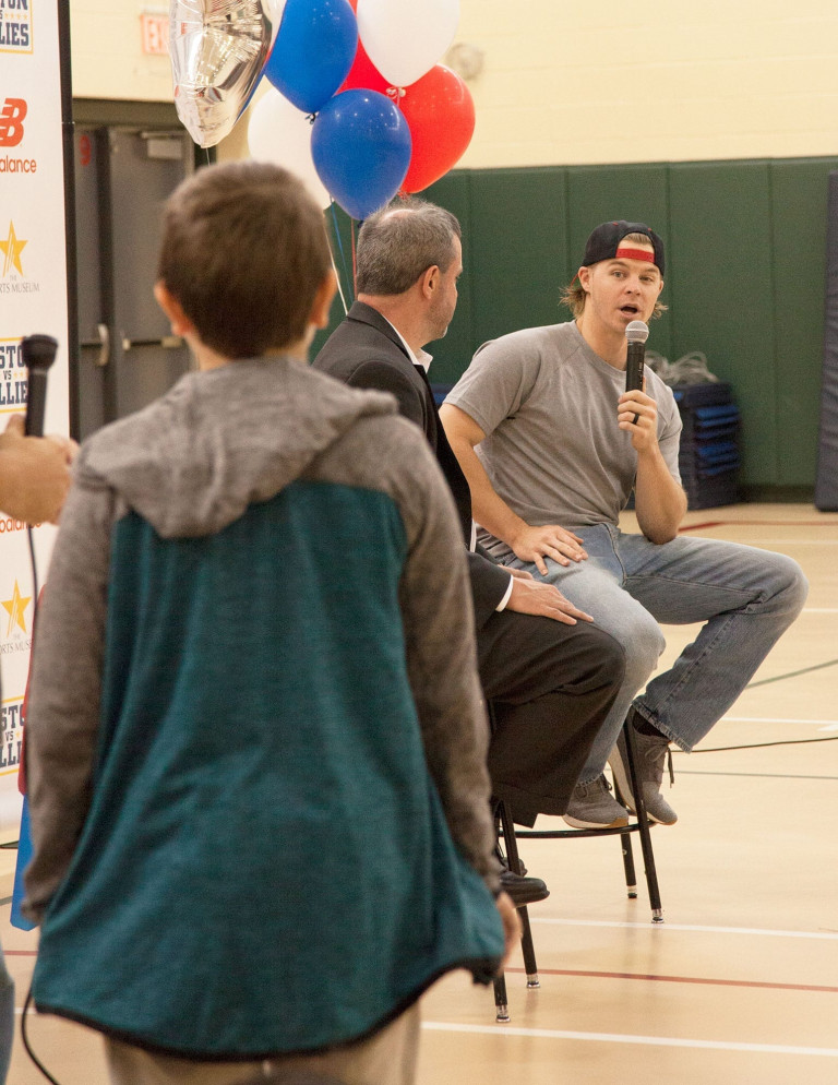 Brock Holt seated on a stool next to another man, talking with a microphone, addressing a child