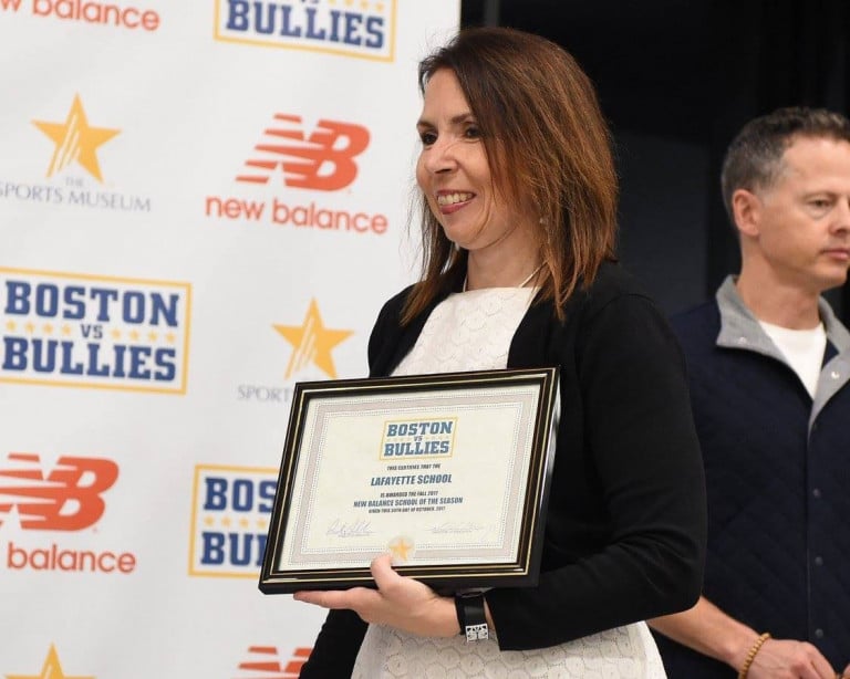 A woman holding a small Boston vs. bullies plaque with another man standing in the background