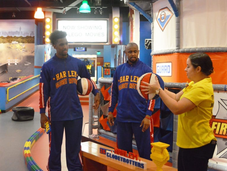 Two Harlem Globetrotters looking at a woman holding a lego basketball