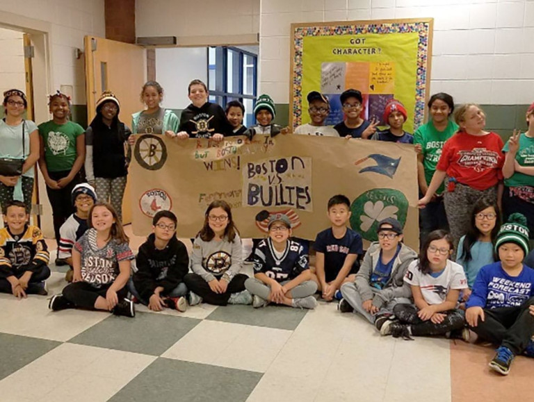 A group of children, some seated in front of a Boston vs. Bullies banner and some standing and holding the banner