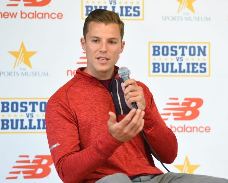 Justin Turri holding a microphone seated in front of a promotional wall