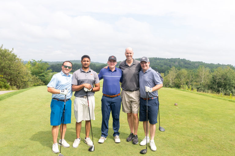 Five men at a golf course smile into the camera.