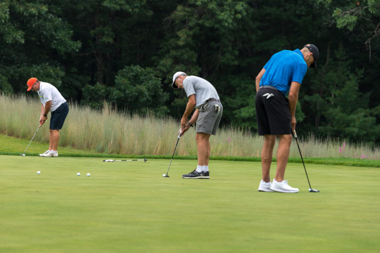Three golfers on the putting green lining up their shots.