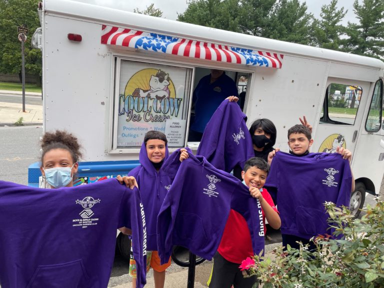 A group of students in front of ice cream truck holding purple Stand Strong sweatshirts.
